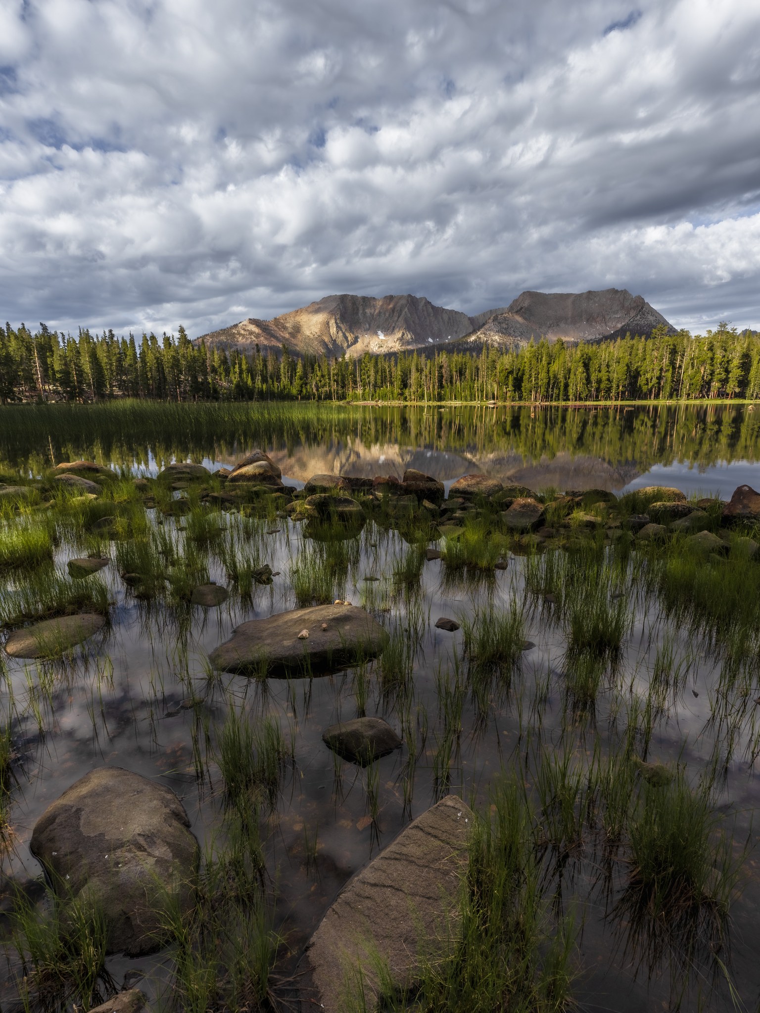 Moraine Lake on the High Sierra Trail at sunrise, the Kaweah Peaks reflected in still water above a grassy shoreline