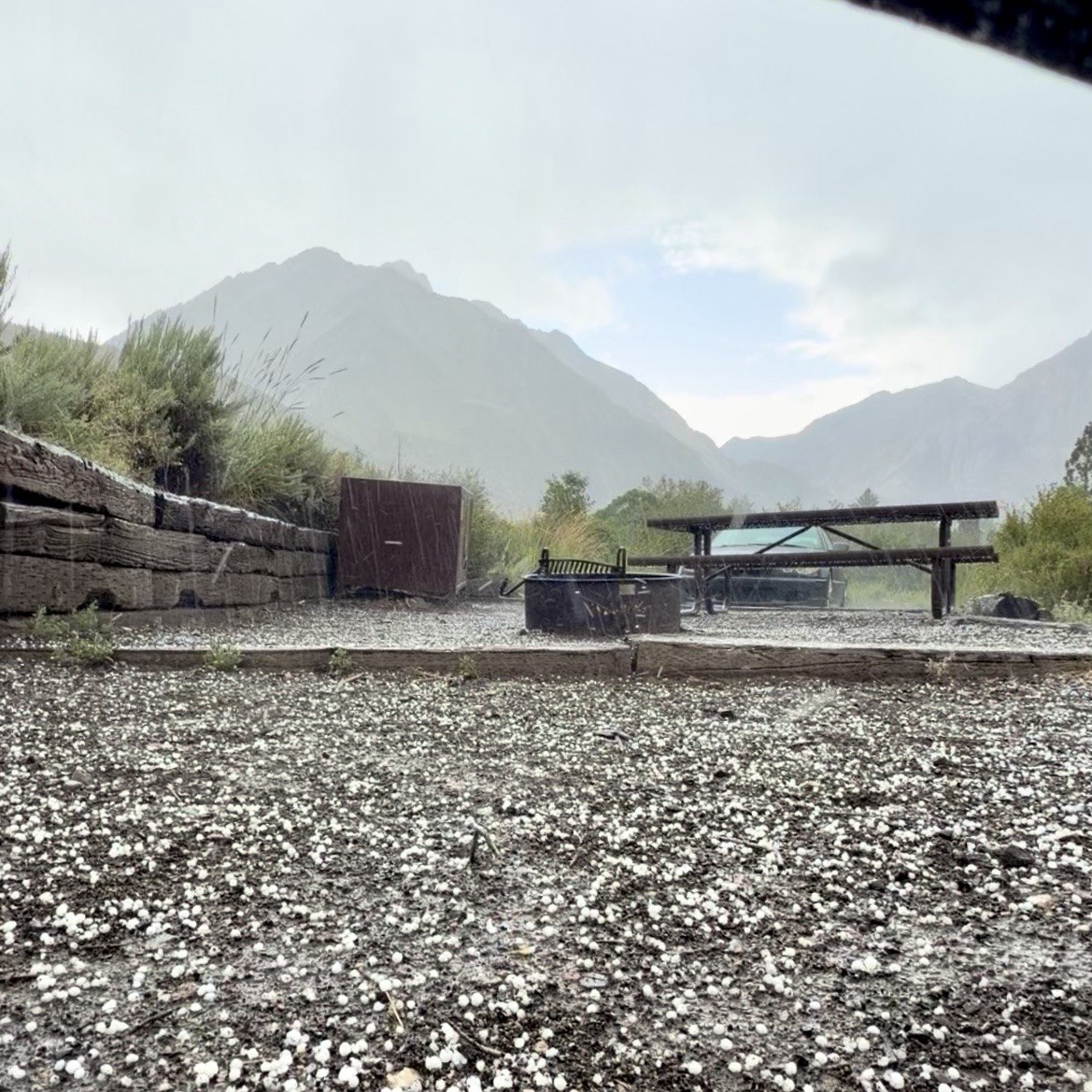 Hail covering the ground at a Convict Lake campsite during a summer storm, picnic table and mountains in the background