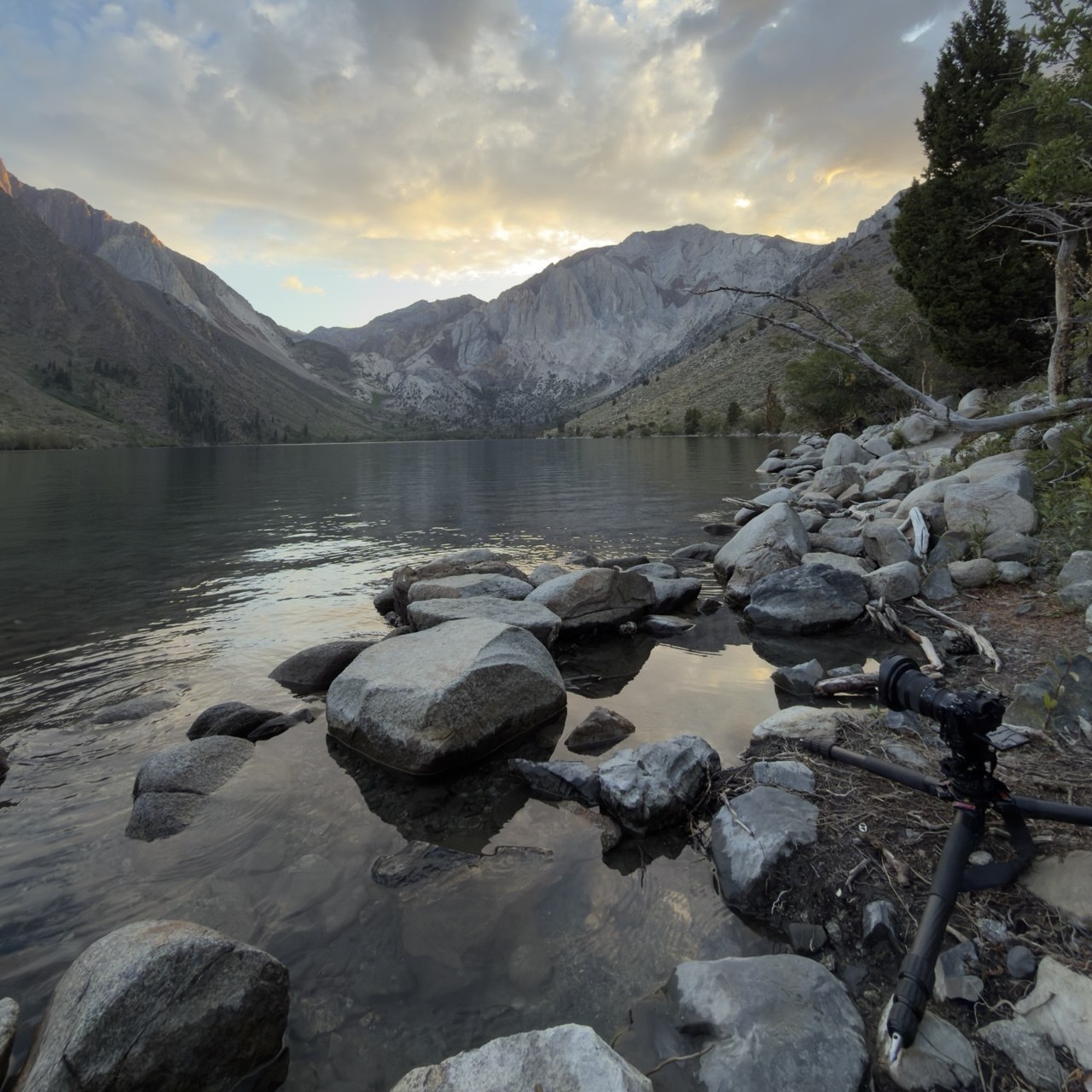 Boulders on the shore of Convict Lake at evening with a camera on a tripod, Mount Morrison and Laurel Mountain across the water under clouds