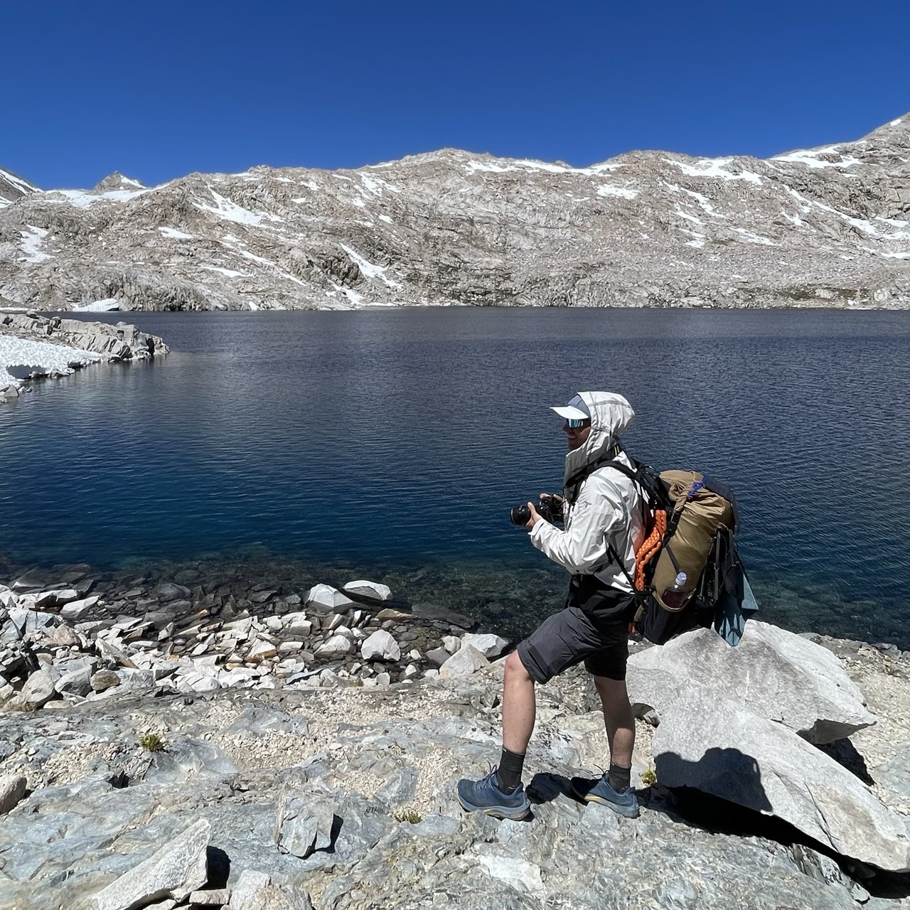 Photographer with a camera from a Peak Design Capture clip beside an alpine lake on the climb to Muir Pass on the John Muir Trail
