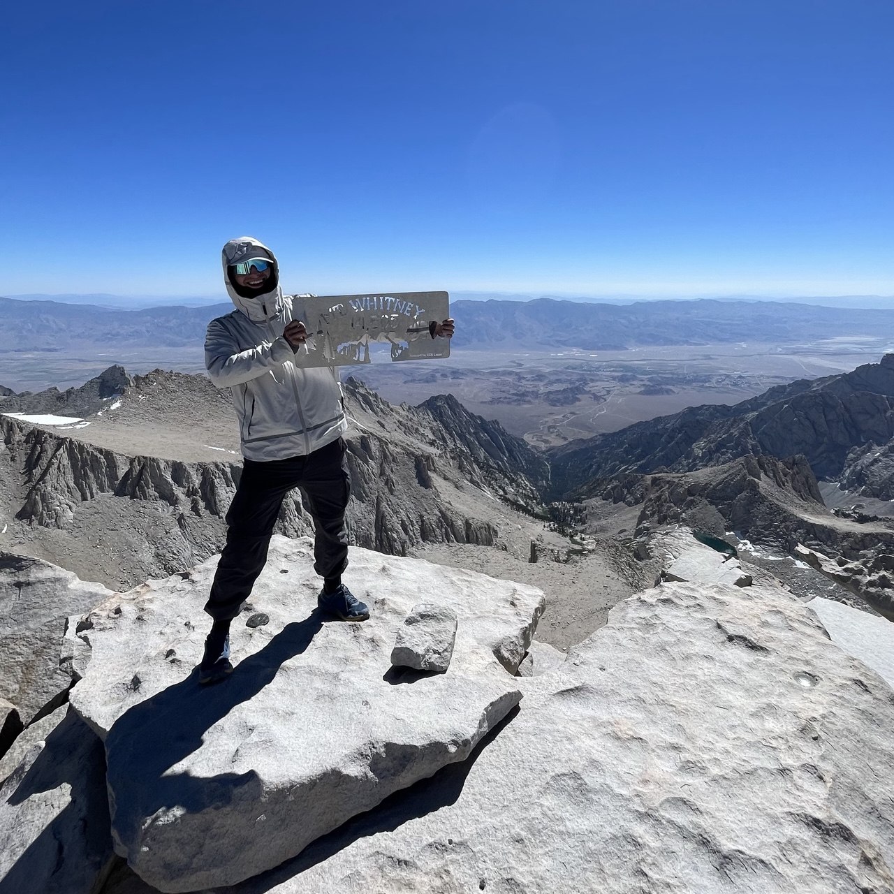 Hiker holding the Mount Whitney summit sign at 14,505 feet on the second day of a northbound John Muir Trail thru-hike