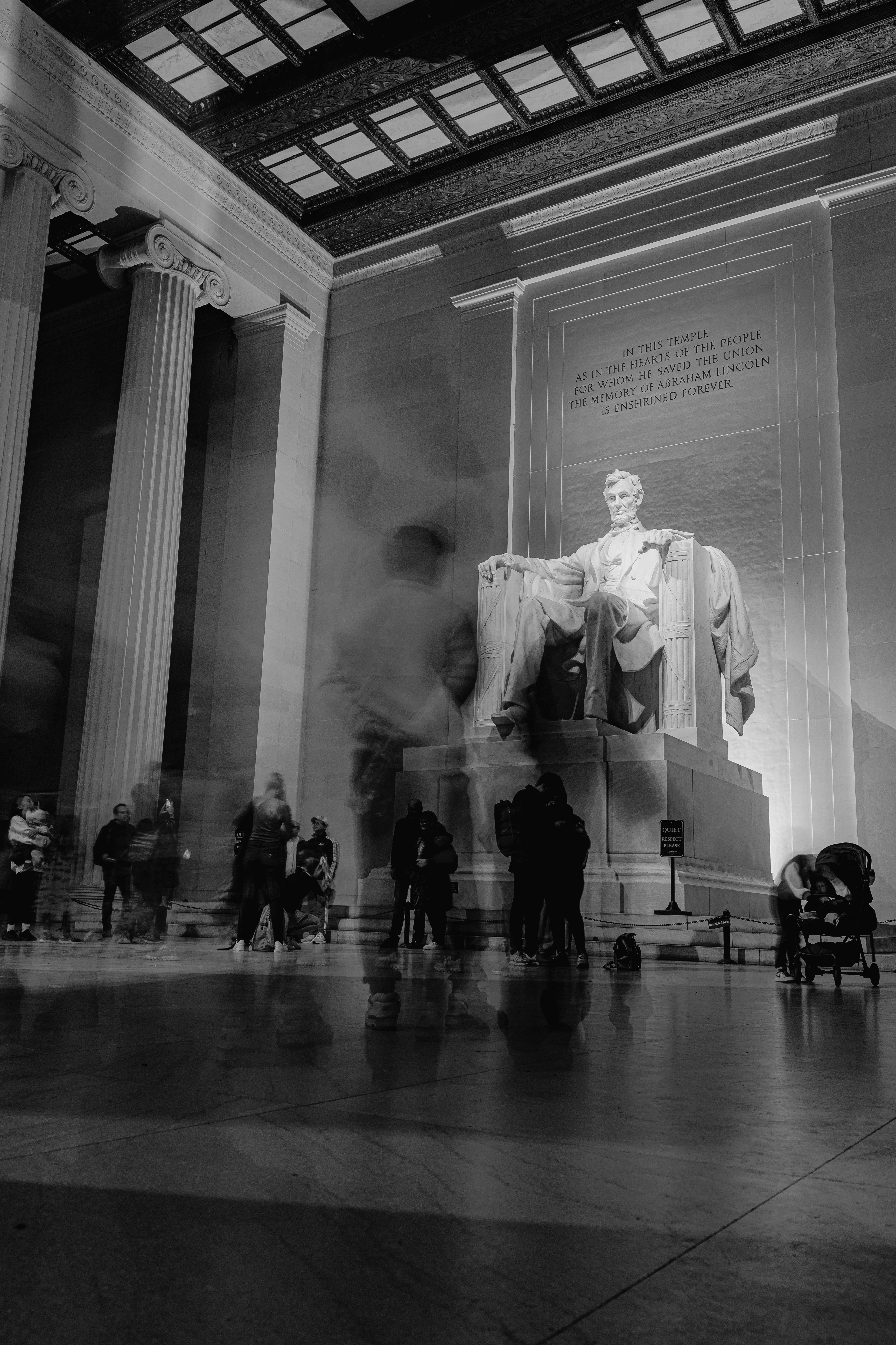 Long-exposure black-and-white photo of the Lincoln Memorial statue with constantly passing visitors