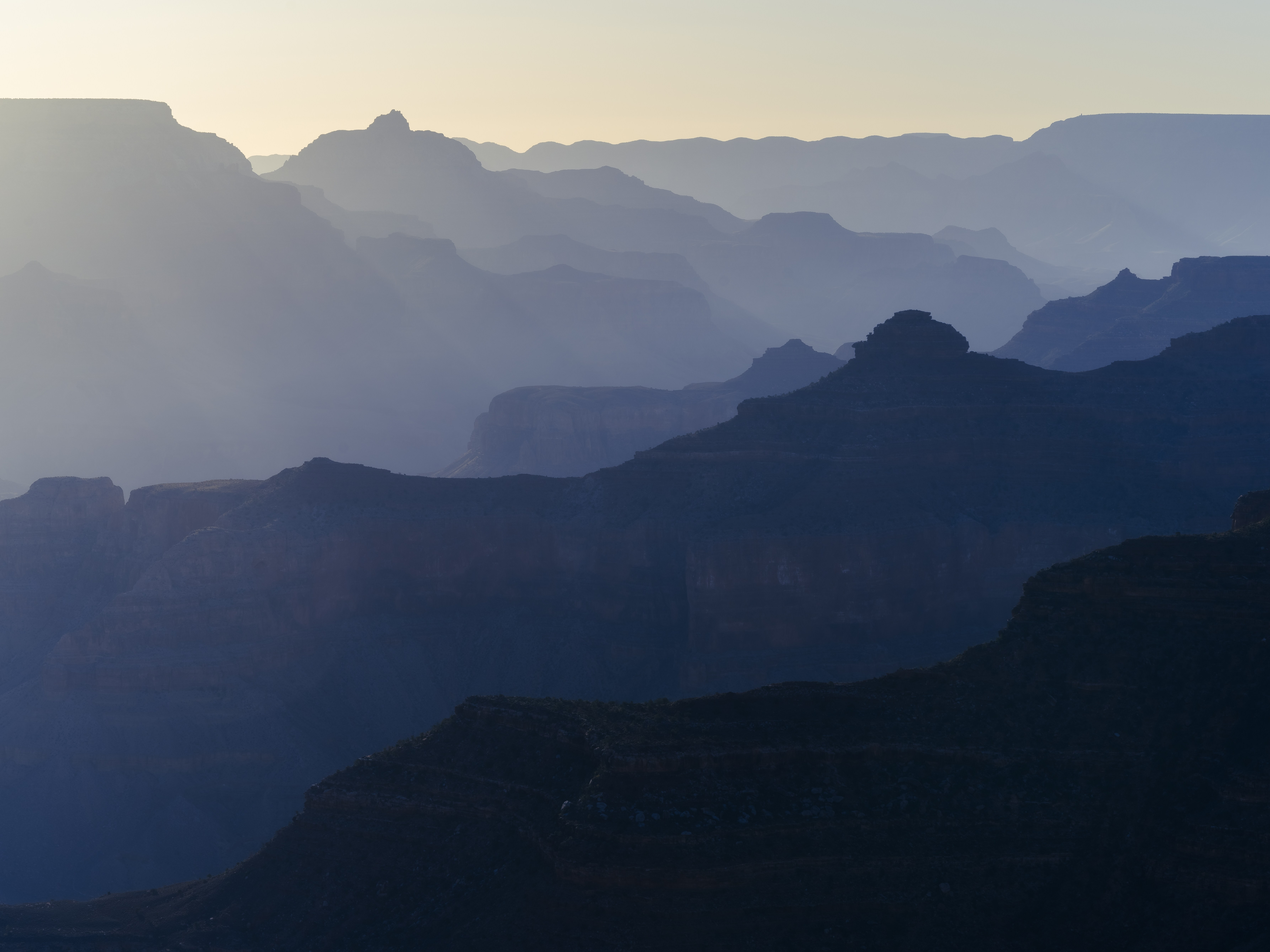 Layered ridgelines of the Grand Canyon fading into morning haze, with O'Neill Butte seen from Hopi Point at sunrise.