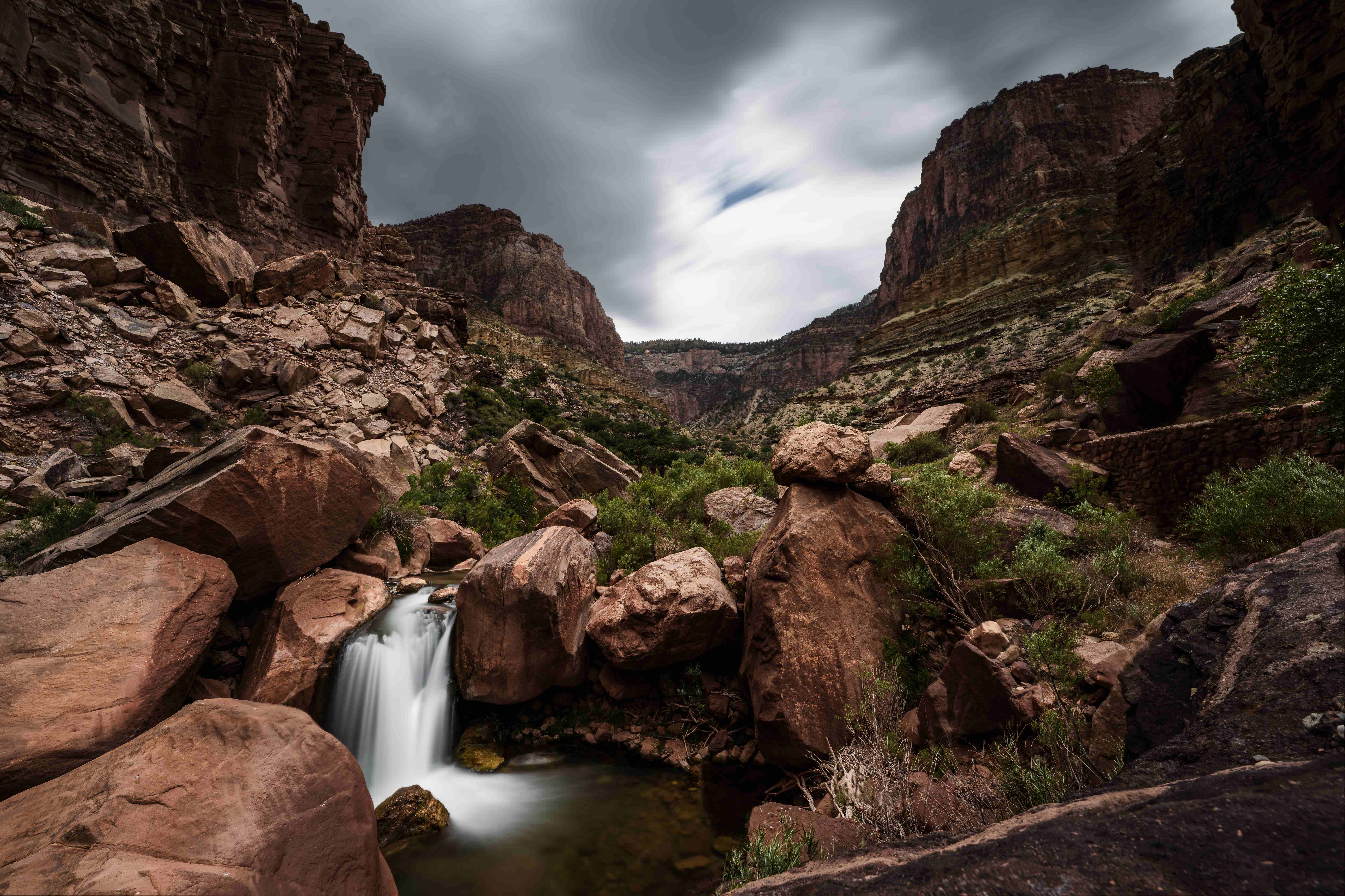 Wide-angle long-exposure view of Split Rock Falls, with storm clouds streaking across the sky above the canyon walls.