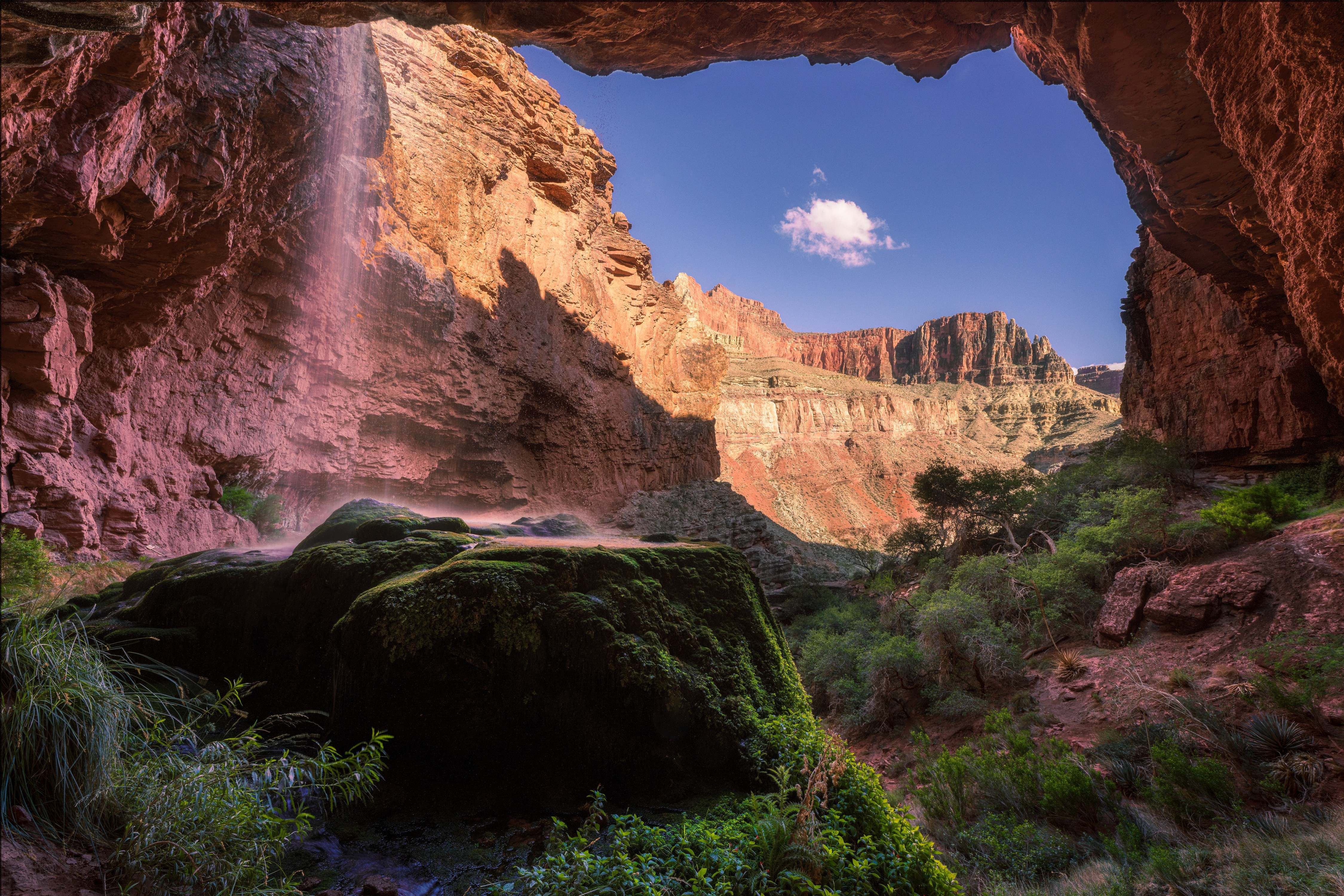 A view from inside the alcove behind Ribbon Falls, a moss-covered rock in the foreground framed by the cave mouth.