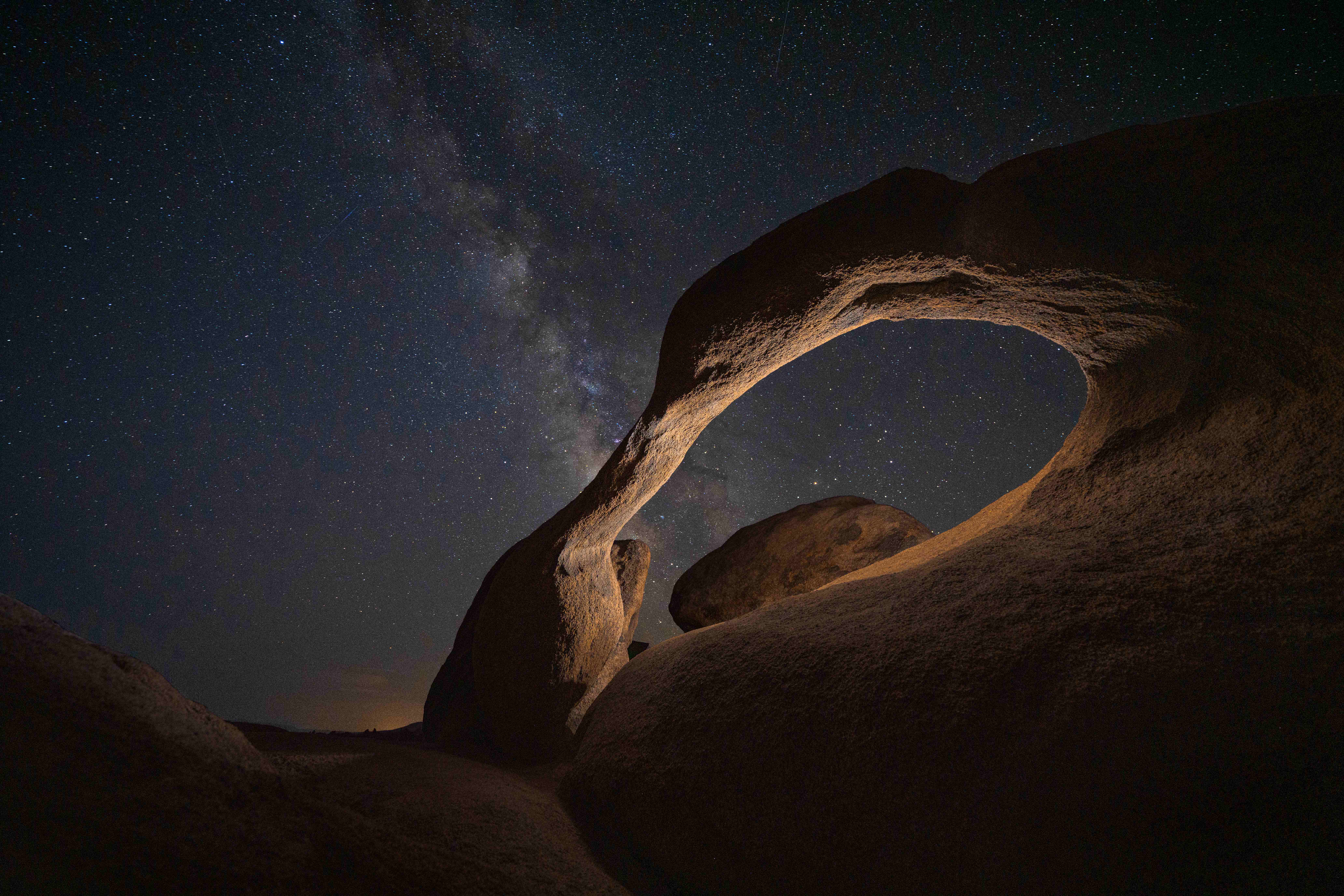Mobius Arch in the Alabama Hills at night, its inner curve lit by headlamp, the Milky Way rising through the arch.